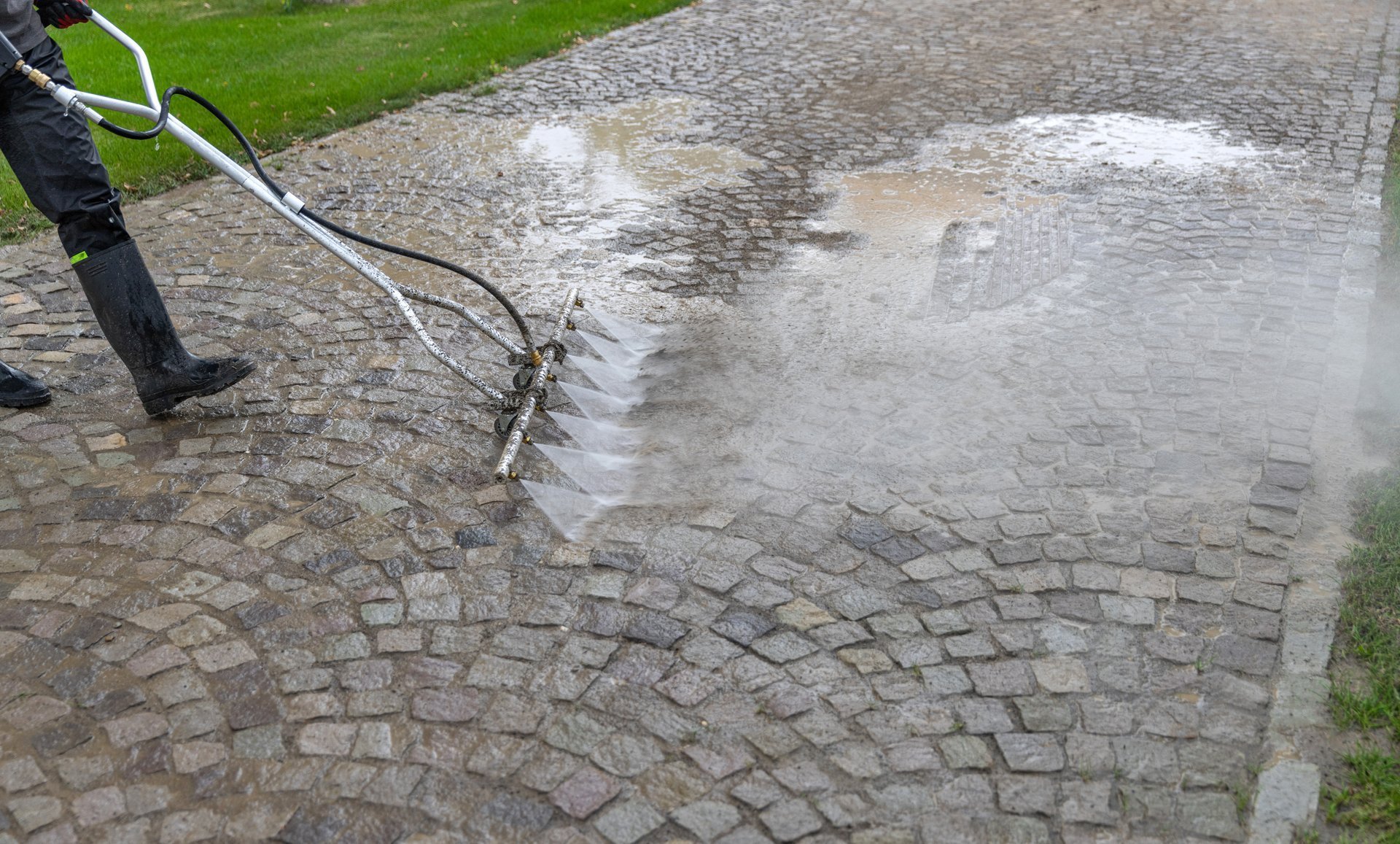 Cleaning service worker washing cobblestone pavement with pressure washer