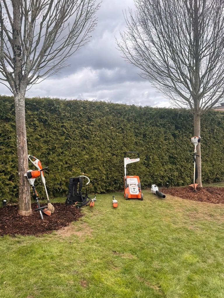 Professionelle Gartenarbeit mitipment zwischen Bäumen und Hecke